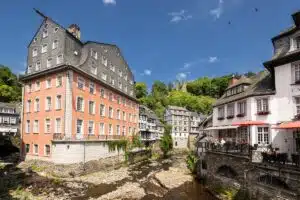 monschau bezienswaardigheden. het rode huis in het centrum van monschau aan het water met andere mooie gebouwen met op de achtergrond de heuvels