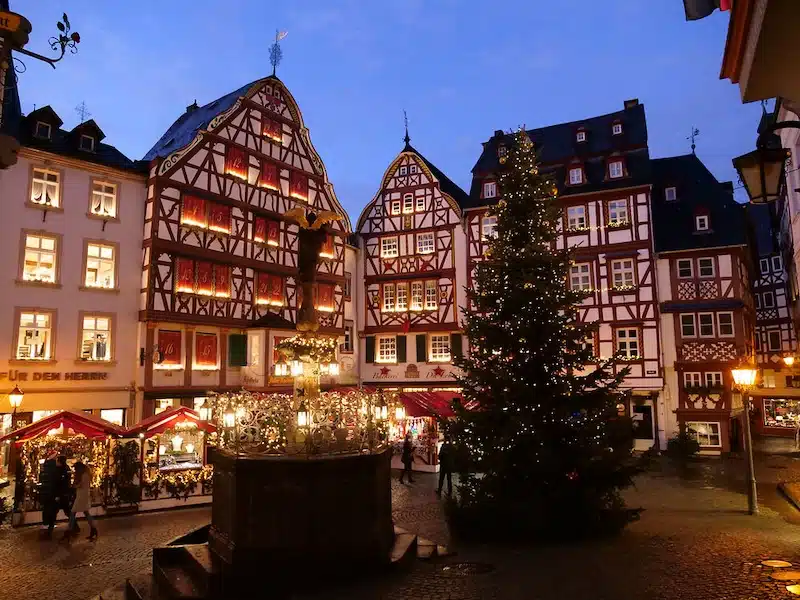 kerstmarkt in Bernkastel Kues. Plein met verlichte en gezellige kraampjes in het centrum omringd door verlichte vakwerkhuizen. Een grote kerstboom met lampjes maken het compleet